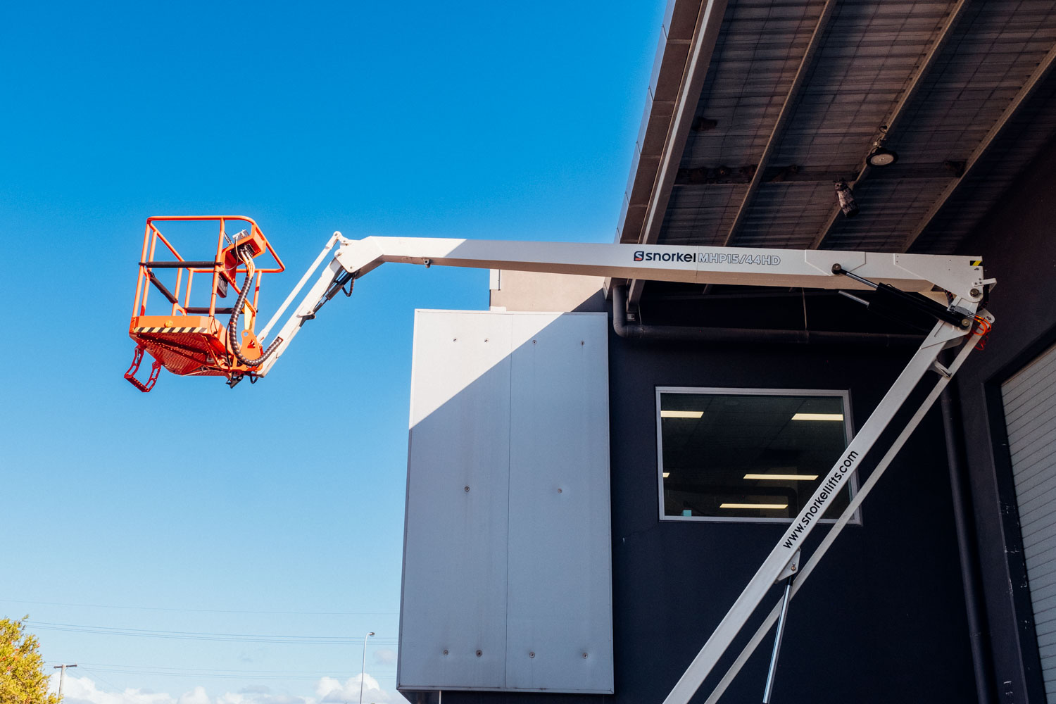 Snorkel boom lift with its orange platform raised high beside a commercial building