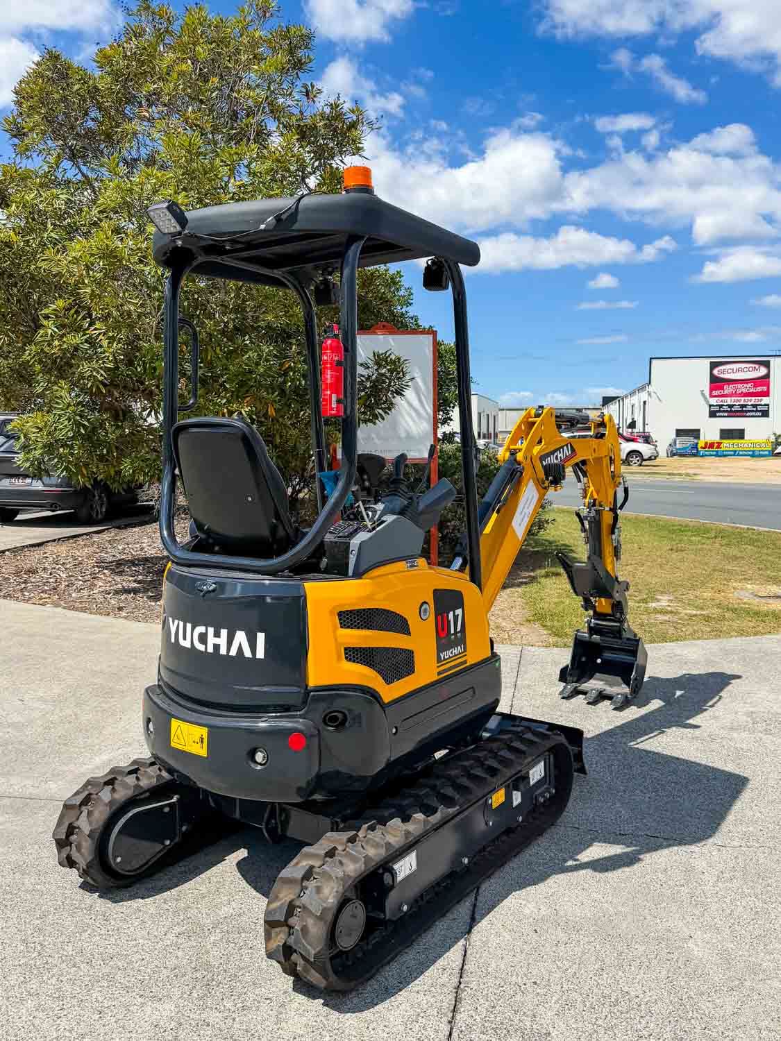 Front three-quarter view of a brand new Yuchai mini excavator with boom raised, parked on site in Brisbane